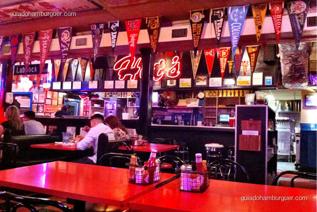 Ambiente super decorado com bandeiras de times, mesas de fórmica e luminoso em neon - Hut's Hamburgers